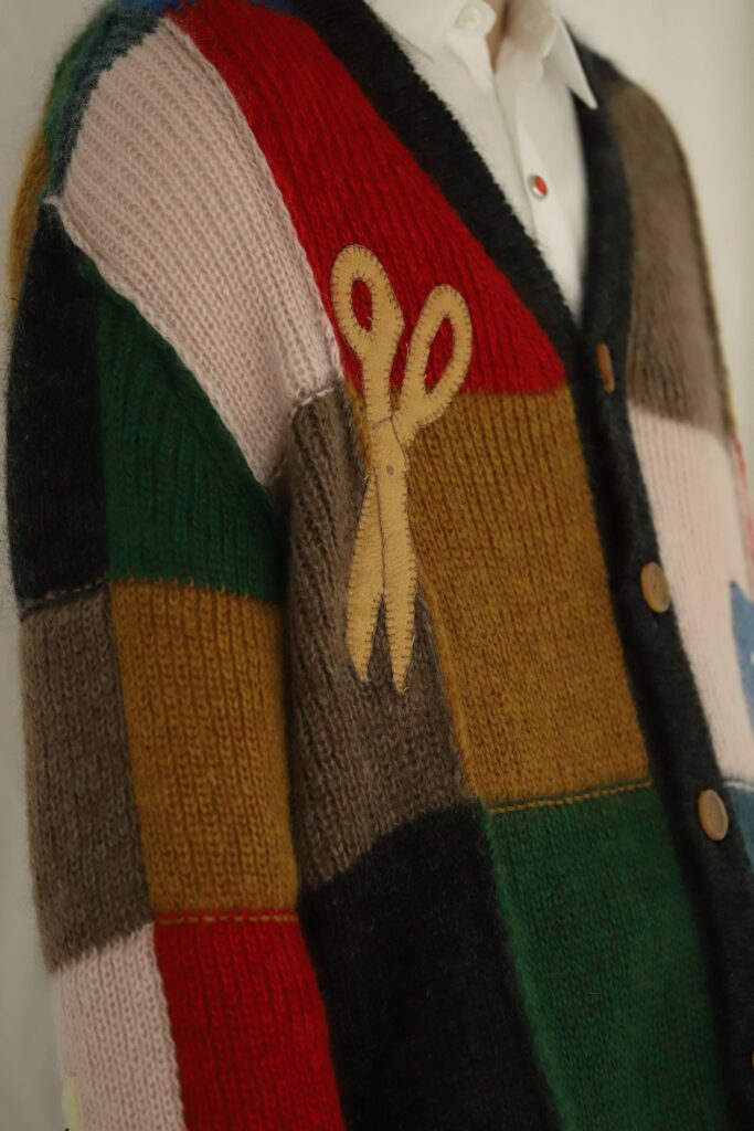 khoki21aw
Y cardigan knit
パッチワークが特徴のカーディガン。
刺繍は一点一点職人による手作業で作るため、 商品ごとに多少の個体差があります。

今回のシーズンにおいてKHOKIが夢中になったのはアメリカンキルト。
1994年に日本ヴォーグ社から出版された『アメリカ/キルトの世界』に掲載された
数々のキルトから影響を受けた。

特に興味深かったのは本来キルトや民芸品はその土地に欠かせない道具や動物、草木をモチーフにすることが多いのだがこの資料には扇子やインド象、東洋モチーフを配したキルトが沢山見受けられた。
どうやら東洋文化への憧れが一つのムーブメントとしてあった1880年ごろのキルトが多い。

ベースのモヘアニットは正直何色指定しているのはわからないぐらい使用している。
配色の切り替え、刺繍も手刺繍。

敢えて丈を短くしてリブを排除、更に縫い代を外出しグランジ風にまとめているもの。
これは本当に工場様含め一緒に作っているニット企画会社さんのお陰だ。
